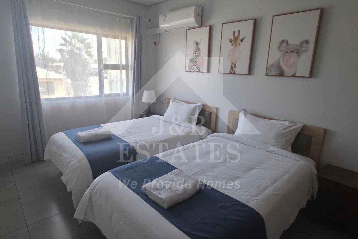 A well-maintained hotel bedroom featuring tiled flooring, a wall-mounted air conditioning unit, and large windows with curtain tracks.