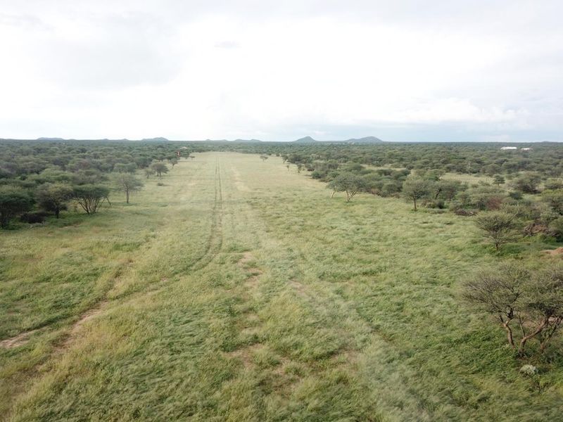 An aerial view of a private grass airstrip set within a vast, natural bushveld landscape.