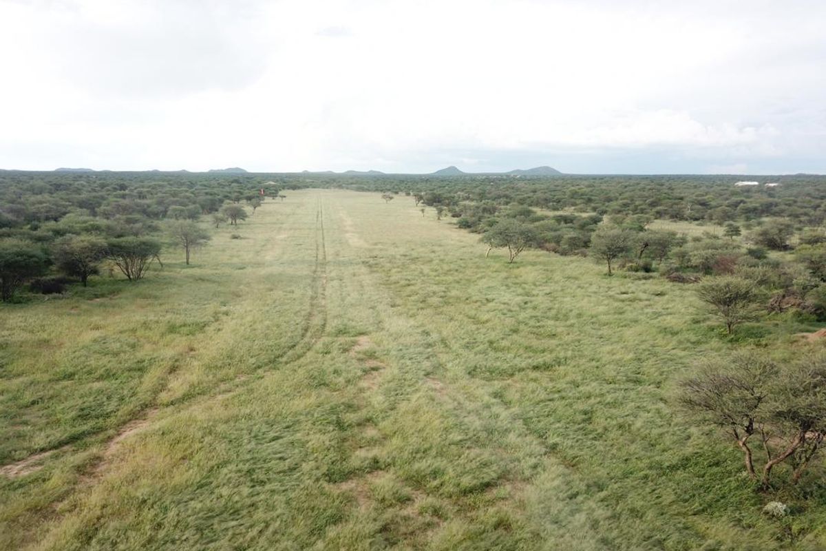 An aerial view of a private grass airstrip set within a vast, natural bushveld landscape.