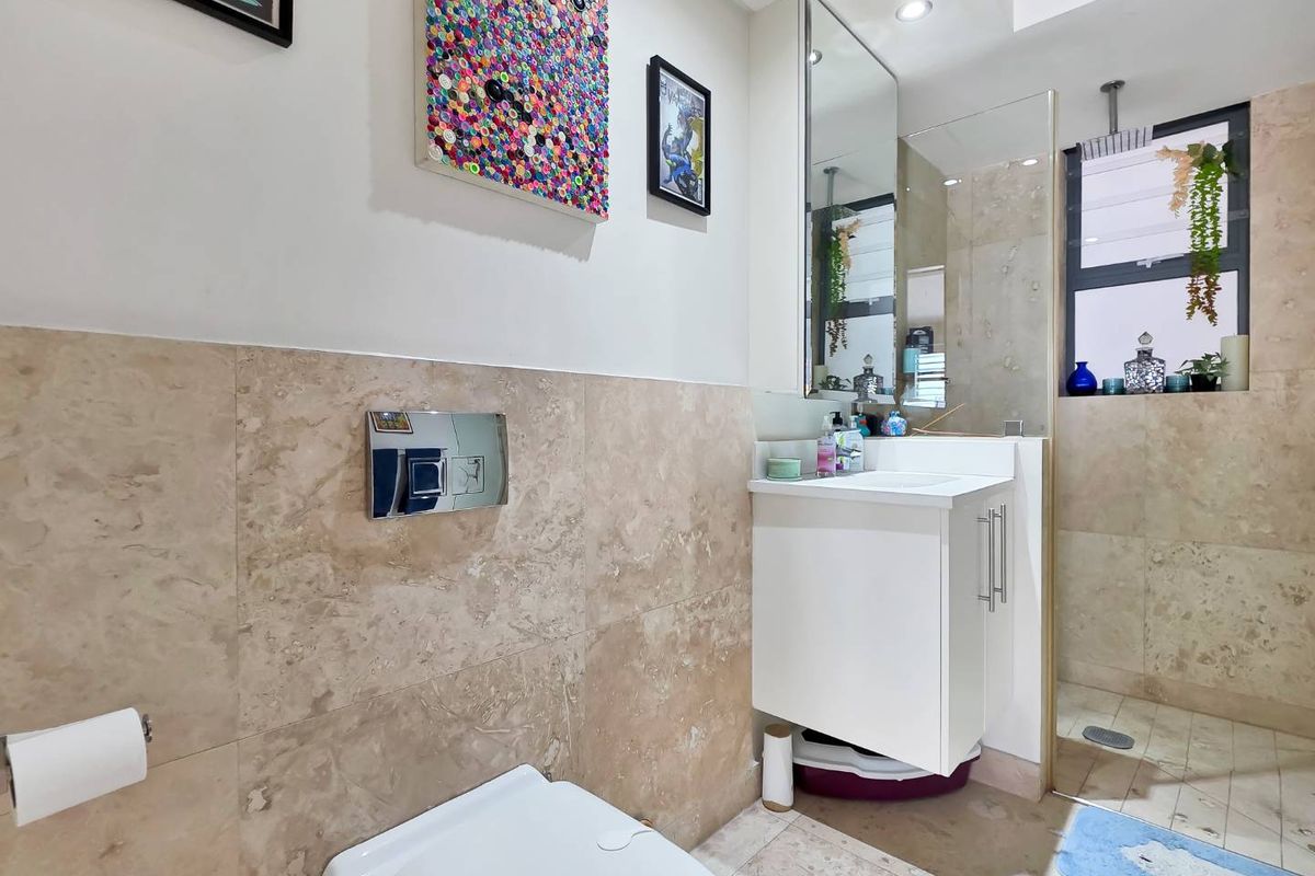 Modern bathroom featuring stone wall and floor tiles, a wall-mounted toilet with chrome flush plate, vanity cabinet, and a glass-enclosed shower.