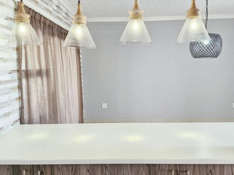 A modern kitchen island featuring wood grain cabinetry, a clean stone countertop, and stylish pendant lighting against a textured feature wall.