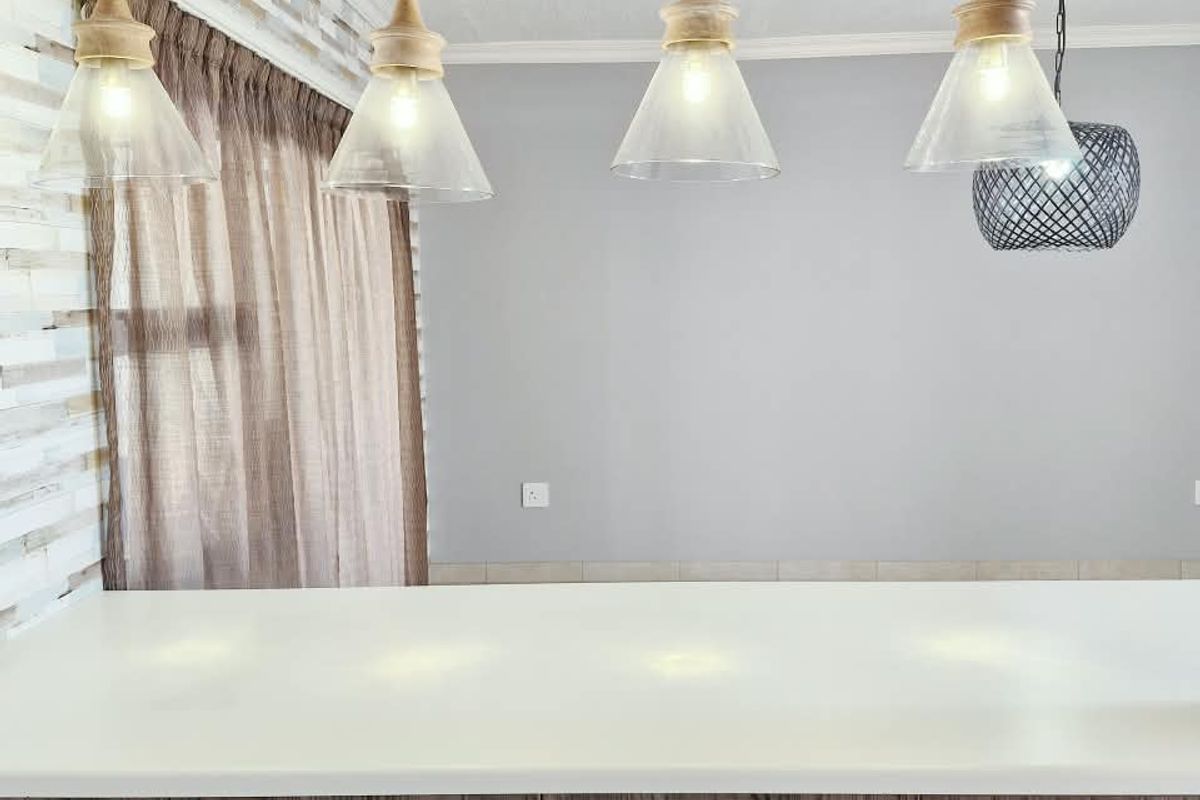 A modern kitchen island featuring wood grain cabinetry, a clean stone countertop, and stylish pendant lighting against a textured feature wall.