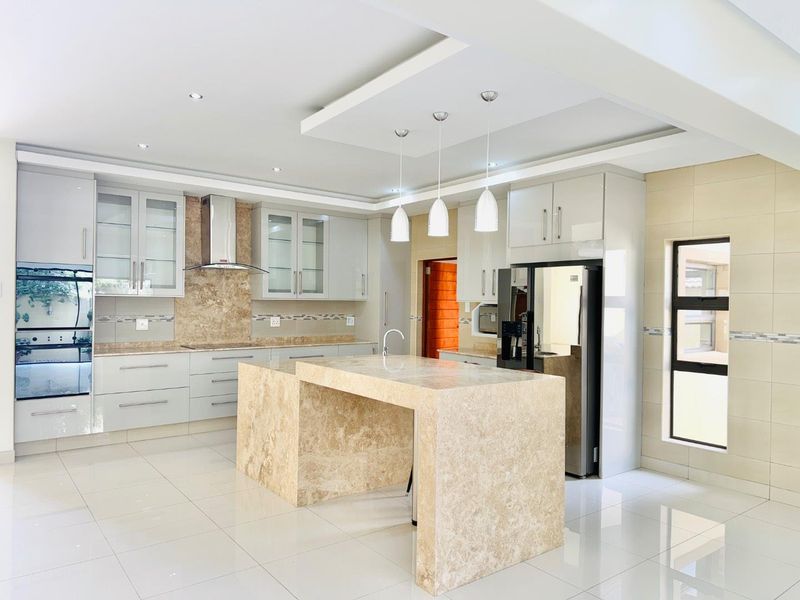 Modern kitchen featuring a large stone island, built-in oven, sleek cabinetry, and high-quality tiled flooring with recessed and pendant lighting.