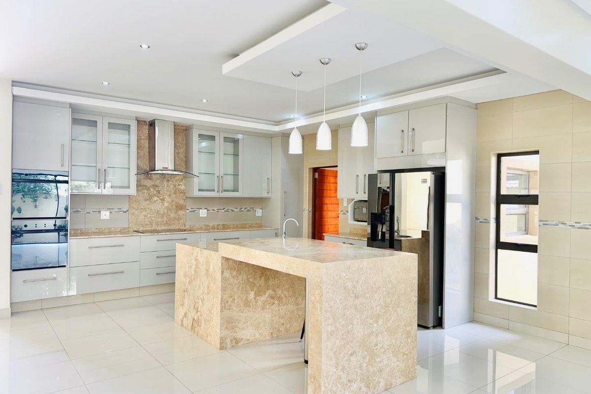 Modern kitchen featuring a large stone island, built-in oven, sleek cabinetry, and high-quality tiled flooring with recessed and pendant lighting.