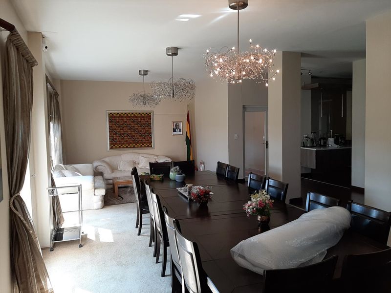 Spacious open-plan living and dining area featuring neutral walls, carpeted flooring, and decorative pendant lighting, with an adjacent kitchen visible in the background.