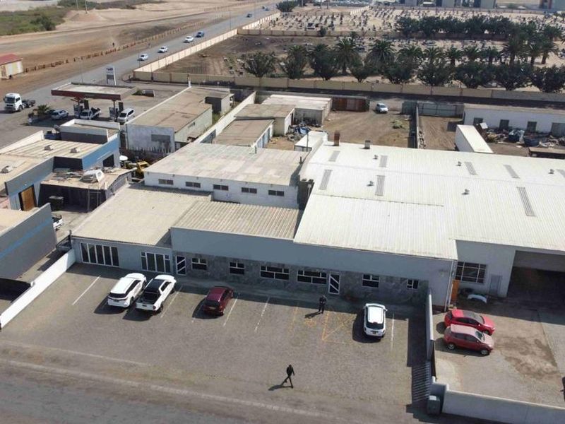 Aerial view of a commercial industrial property featuring a large warehouse building with metal roofing and an adjacent asphalt parking area.
