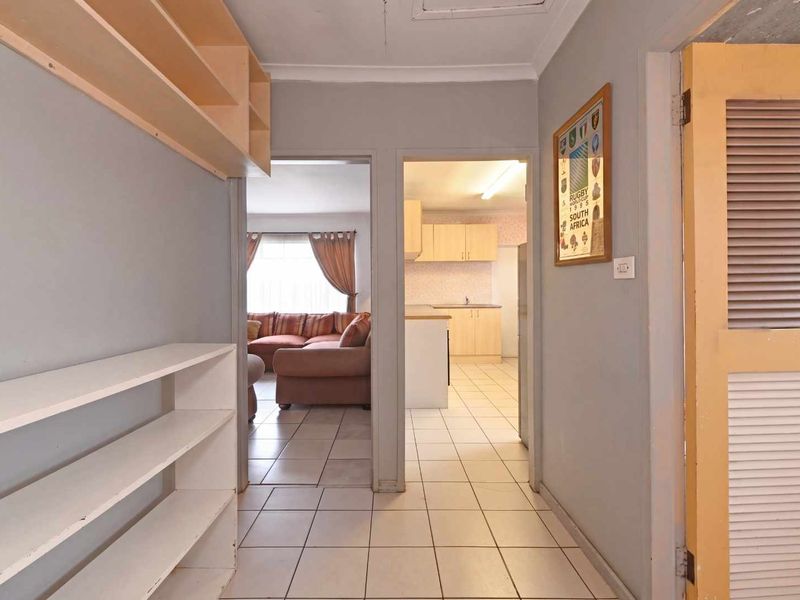 A functional hallway featuring built-in shelving, tiled flooring, and direct access to the adjacent living area and kitchen.
