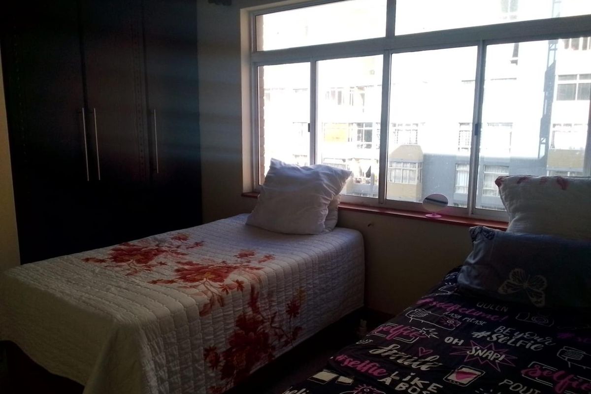 A bedroom featuring built-in cupboards and a large sliding window providing natural light.
