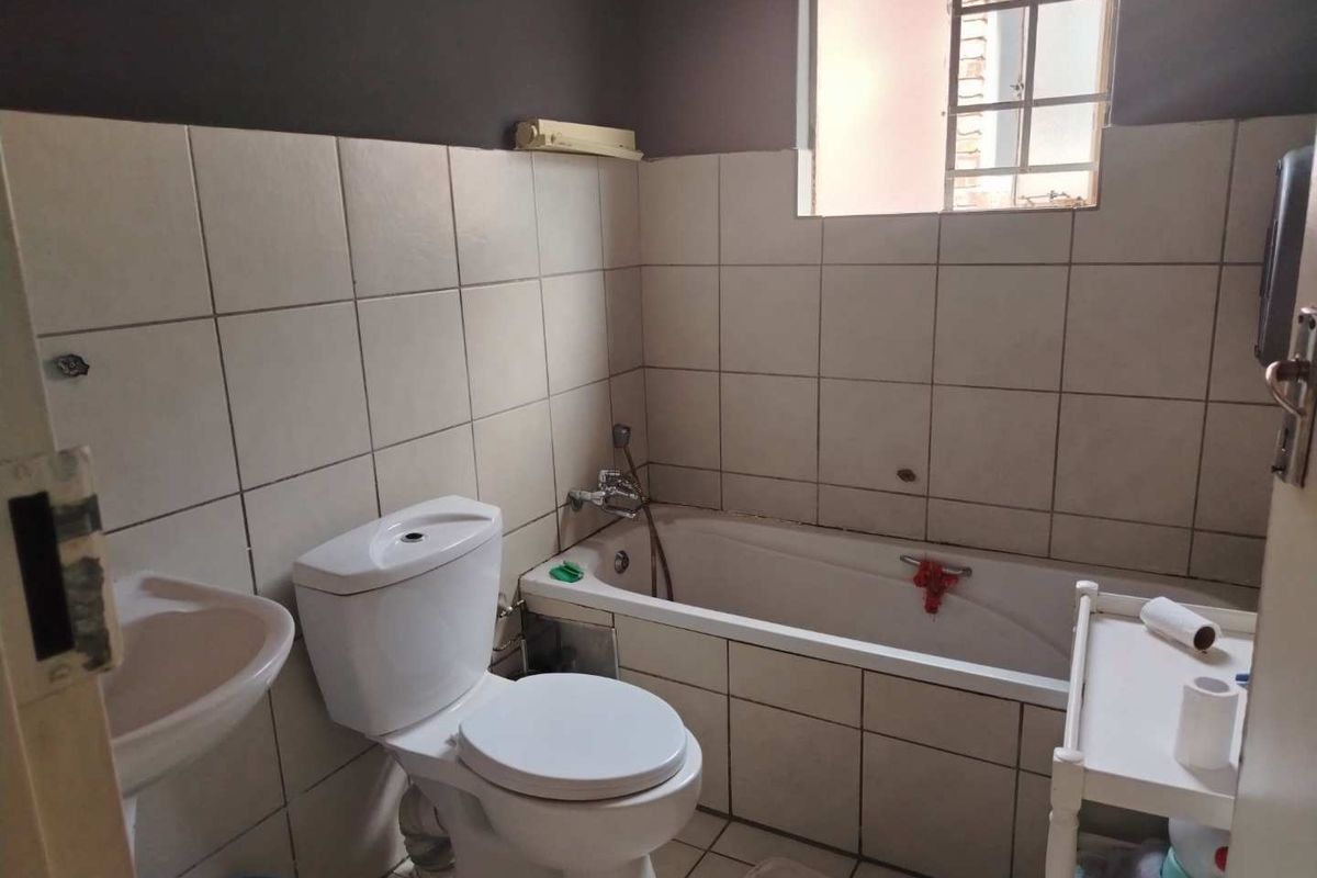 A functional bathroom featuring a bathtub, toilet, and pedestal basin with tiled walls and flooring, requiring some cosmetic maintenance and updates.