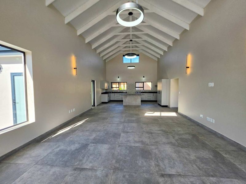 Spacious open-plan living and kitchen area featuring a high vaulted ceiling with exposed rafters, modern tiled flooring, and a central kitchen island.