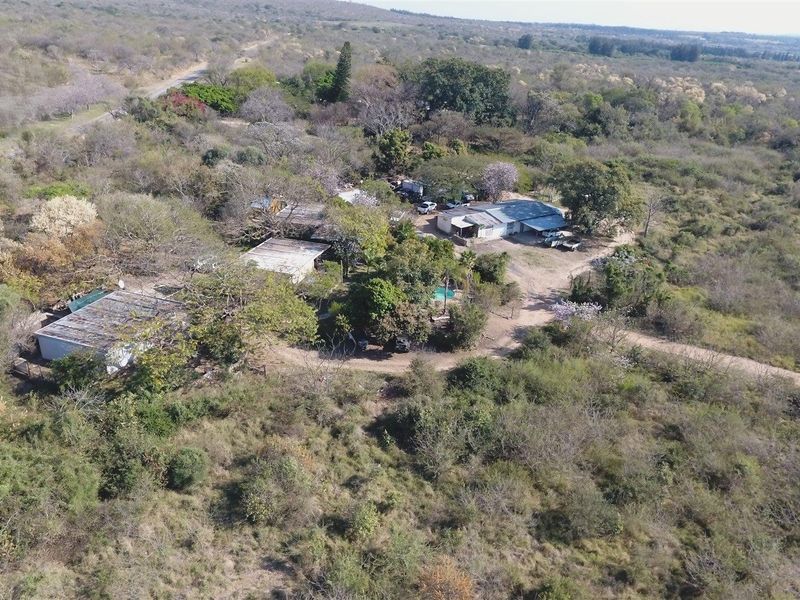 Aerial view of a rural farm property featuring multiple structures with metal roofing, surrounded by extensive natural vegetation and dirt access roads.