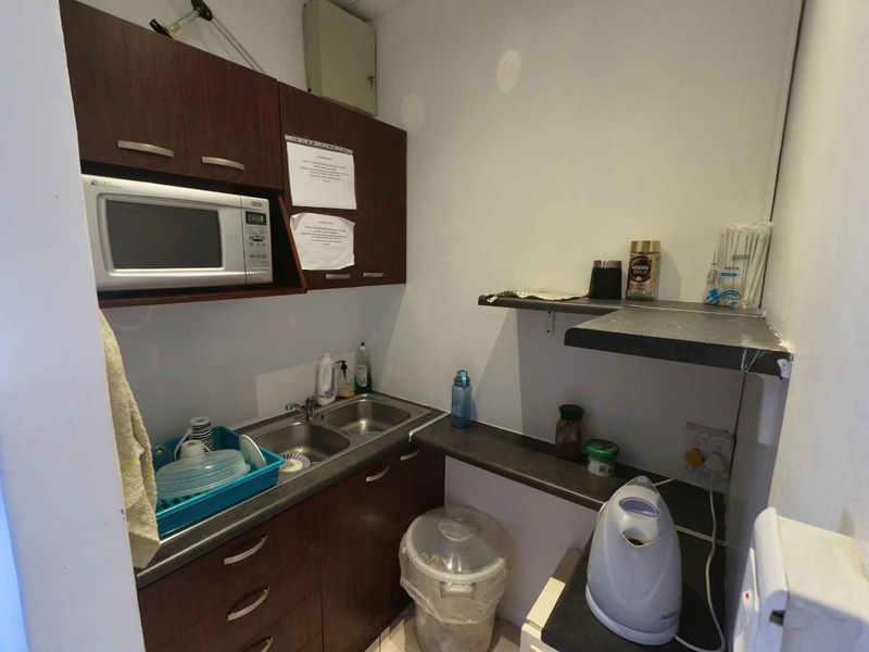 Compact office scullery area featuring dark wood cabinetry, a double stainless steel sink, built-in microwave, and additional wall-mounted storage shelving.