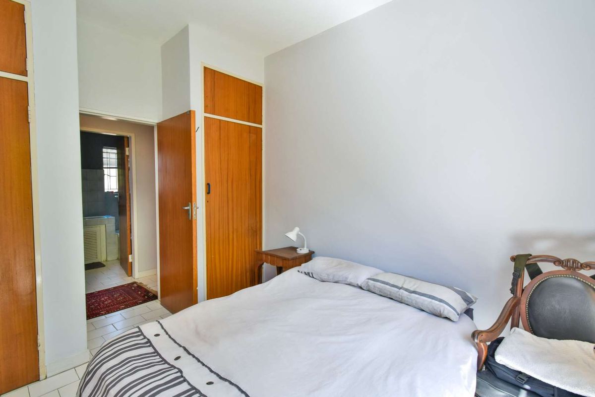 A bedroom featuring built-in wooden cupboards and direct access to an adjoining bathroom with tiled flooring.