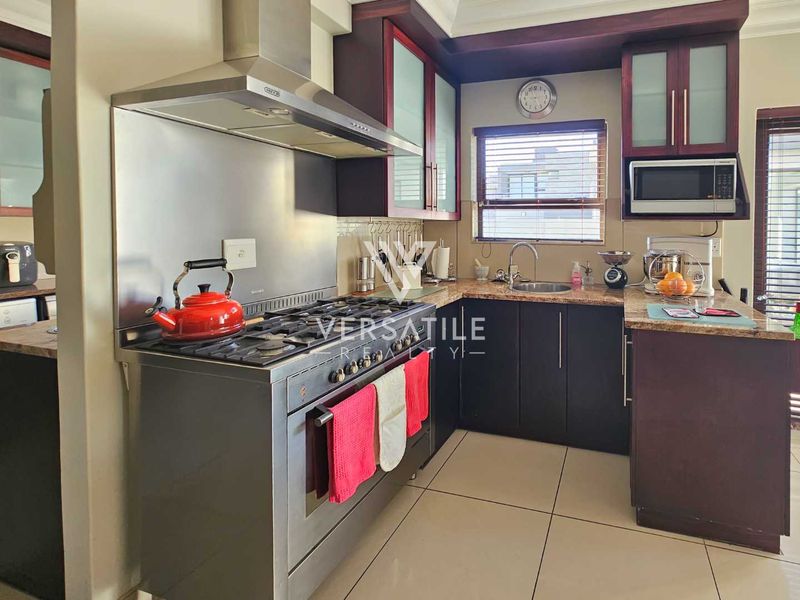 A functional kitchen featuring dark cabinetry, granite countertops, a stainless steel gas stove with extractor fan, and tiled flooring.