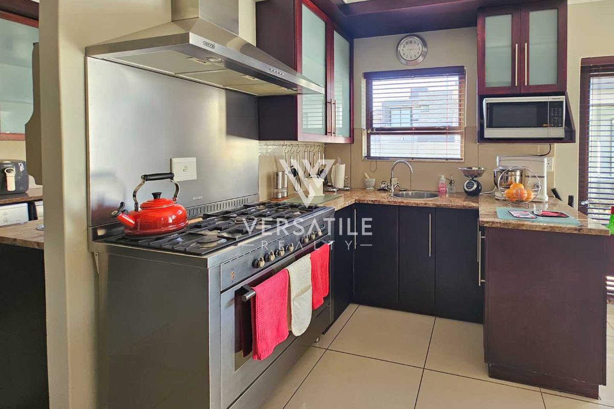 A functional kitchen featuring dark cabinetry, granite countertops, a stainless steel gas stove with extractor fan, and tiled flooring.