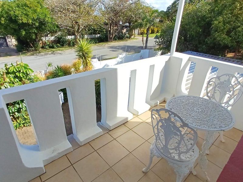 An elevated balcony featuring tiled flooring and a solid white balustrade, offering an open view of the street and surrounding greenery.