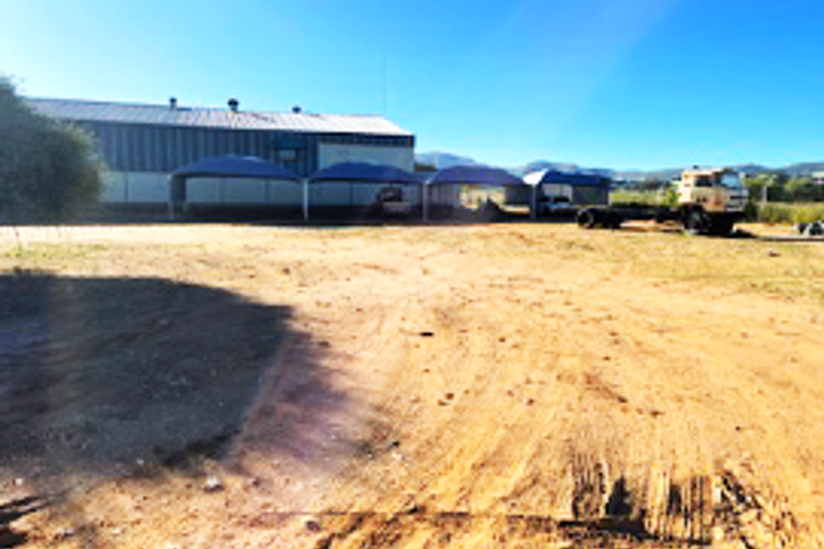 Exterior view of a commercial warehouse building featuring a large unpaved yard area and multiple covered parking bays.