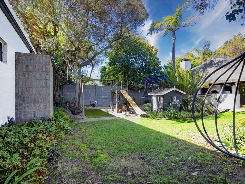 A private rear garden featuring a lawn, mature trees, brick and concrete boundary walls, and an outdoor fireplace area.