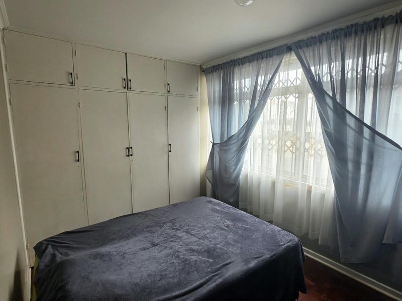 A bedroom featuring built-in cupboards, parquet flooring, and a window fitted with a security gate.