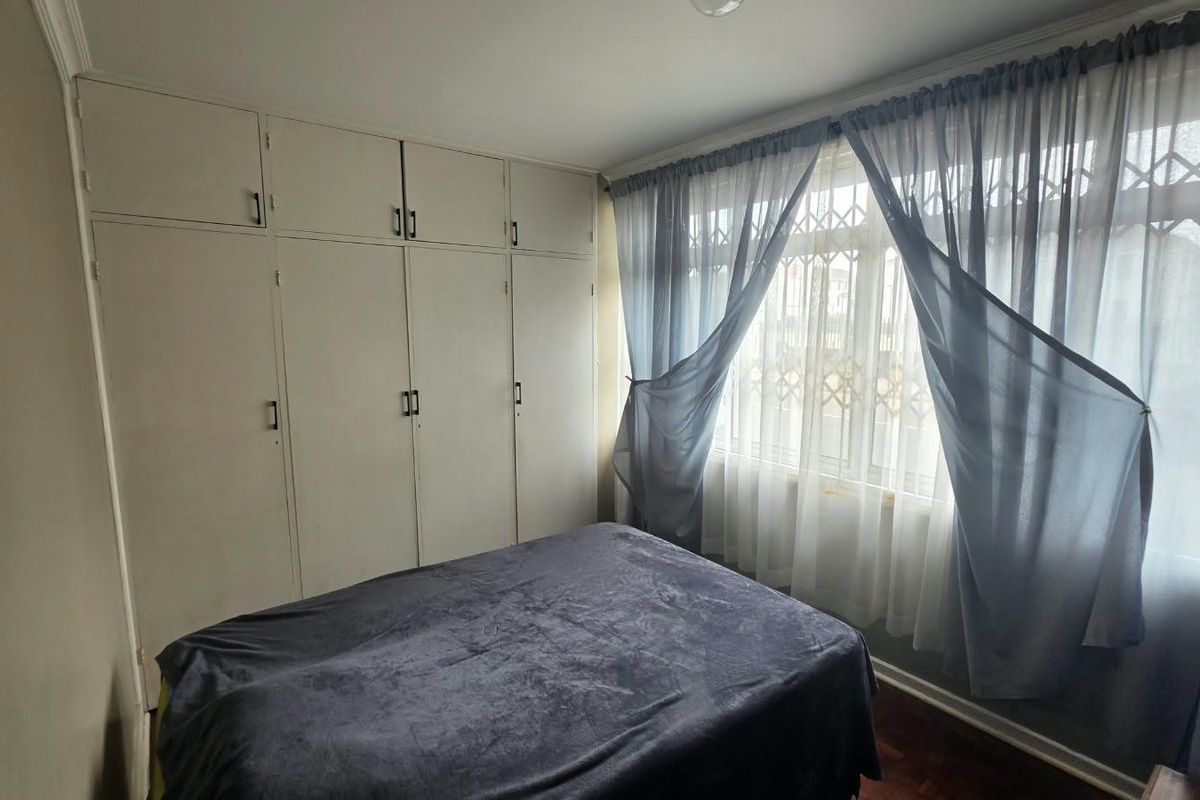 A bedroom featuring built-in cupboards, parquet flooring, and a window fitted with a security gate.