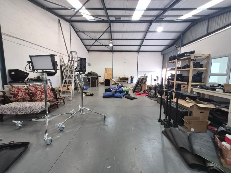 Spacious industrial utility area featuring high ceilings with exposed steel trusses, skylights, concrete flooring, and a large roller shutter door.