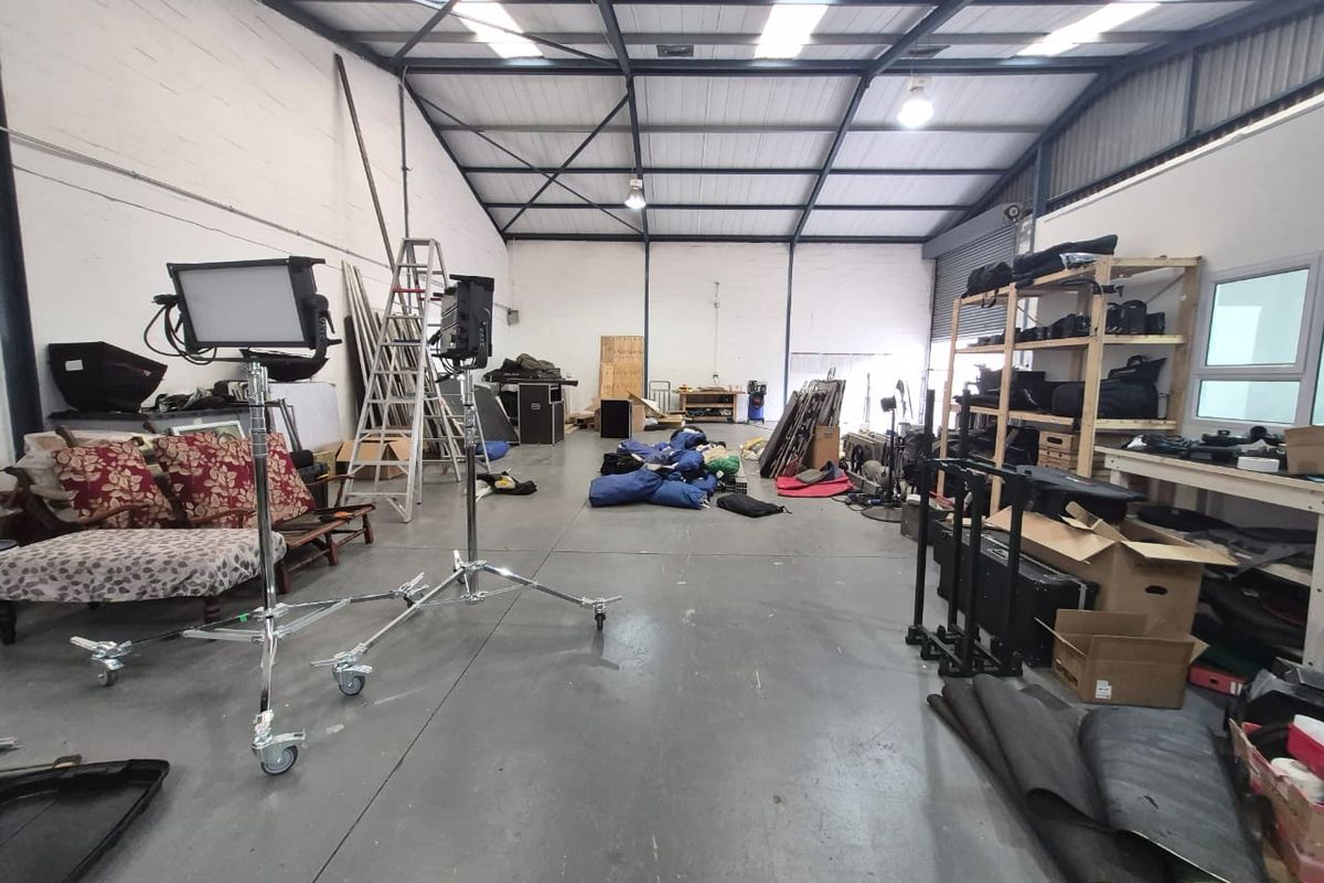 Spacious industrial utility area featuring high ceilings with exposed steel trusses, skylights, concrete flooring, and a large roller shutter door.