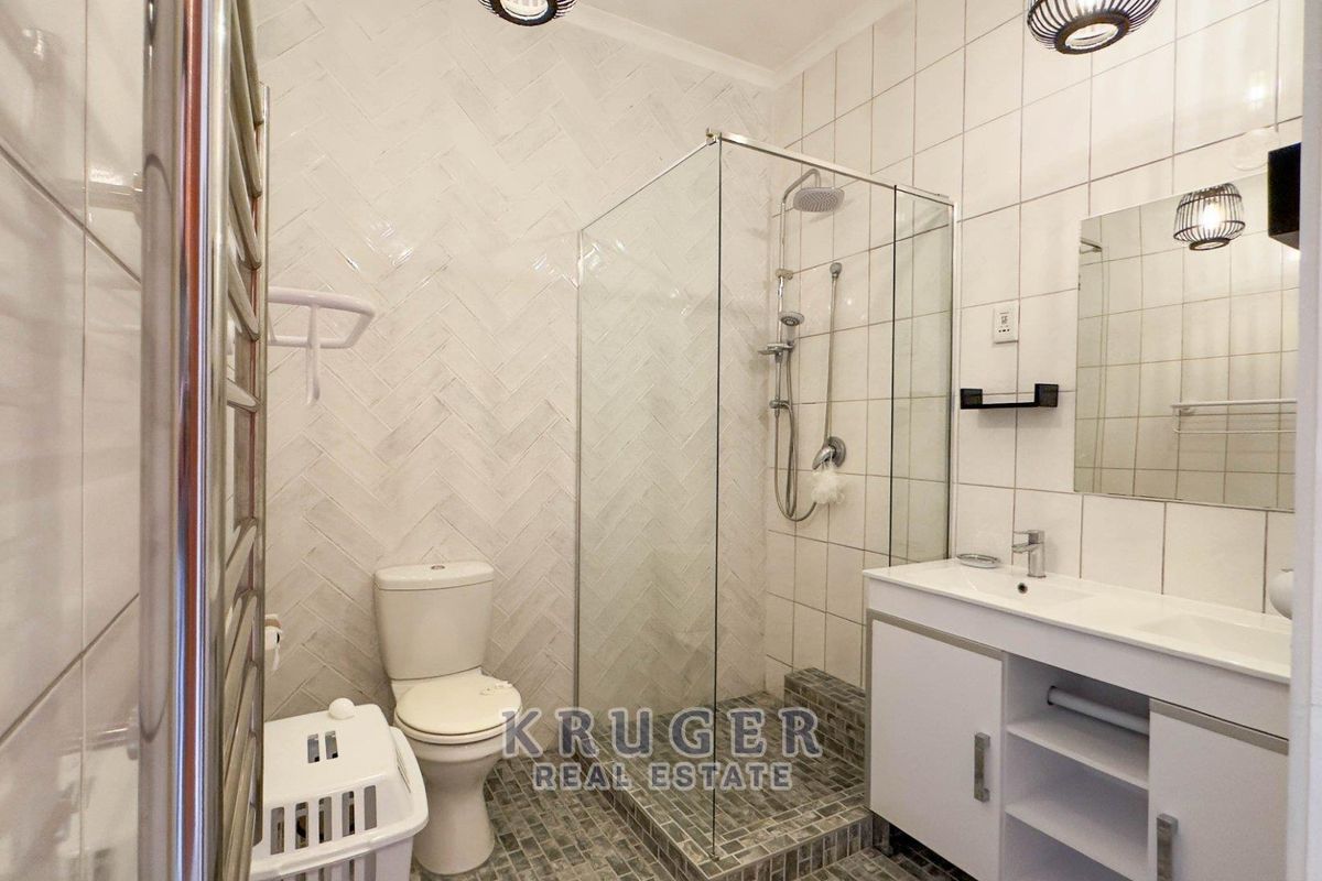 Modern bathroom featuring a glass-enclosed walk-in shower, white vanity with integrated basin, and stylish herringbone wall tiling.