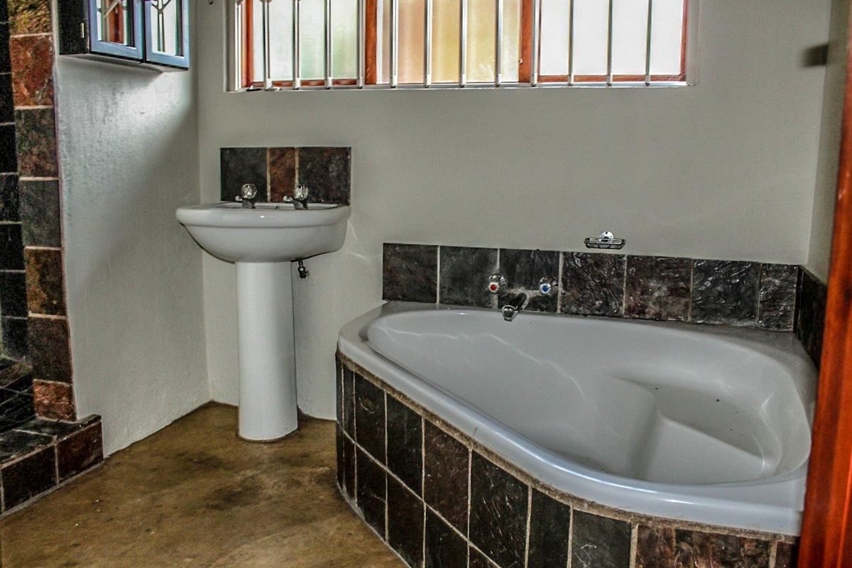 A dated bathroom featuring a corner bathtub and pedestal basin with dark stone-look tiling and security bars on the window.