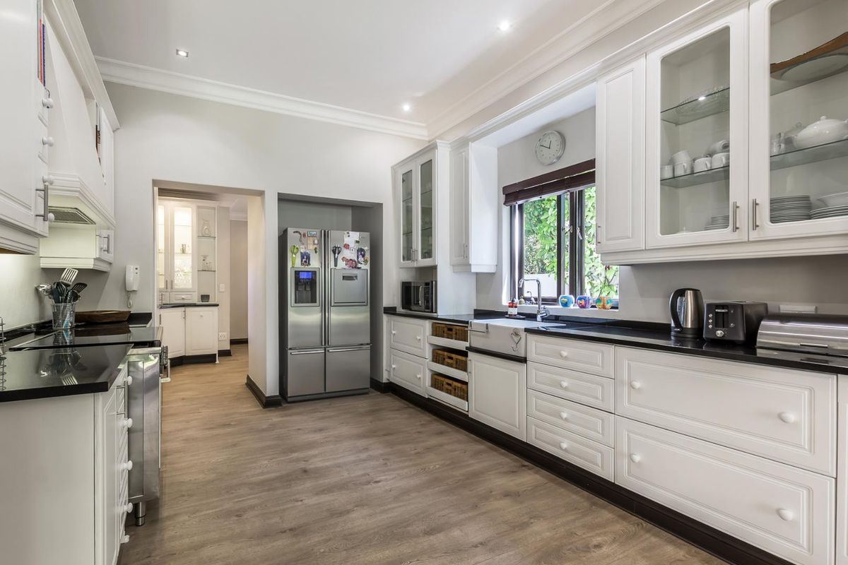 A well-appointed kitchen featuring white cabinetry, dark stone countertops, a farmhouse-style sink, and integrated storage, leading into a secondary scullery area.