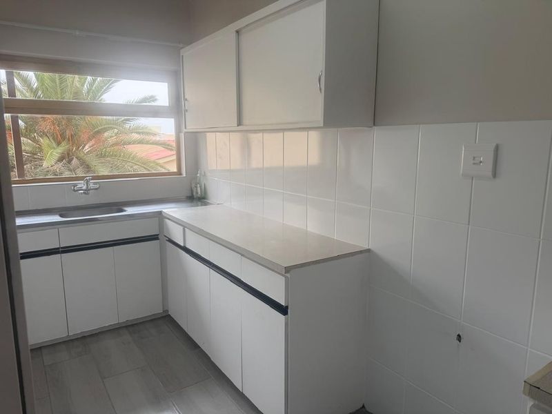 A functional kitchen area featuring white built-in cabinetry, a stainless steel sink, tiled splashbacks, and neutral flooring, offering a clean canvas for updates.