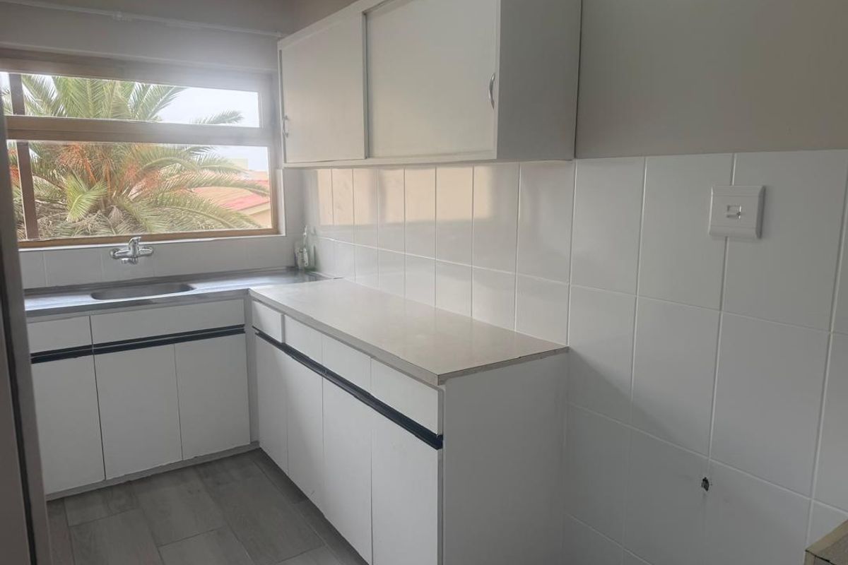 A functional kitchen area featuring white built-in cabinetry, a stainless steel sink, tiled splashbacks, and neutral flooring, offering a clean canvas for updates.