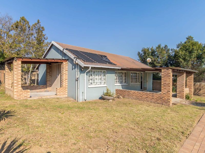 Rear view of a detached house featuring a brick-pillared patio, tiled roof, and an integrated solar water heating system set within a garden.