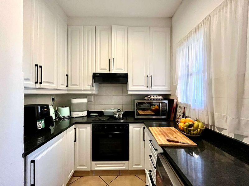 A compact, functional kitchen featuring white cabinetry, black granite countertops, and integrated cooking appliances with a tiled backsplash and floor.