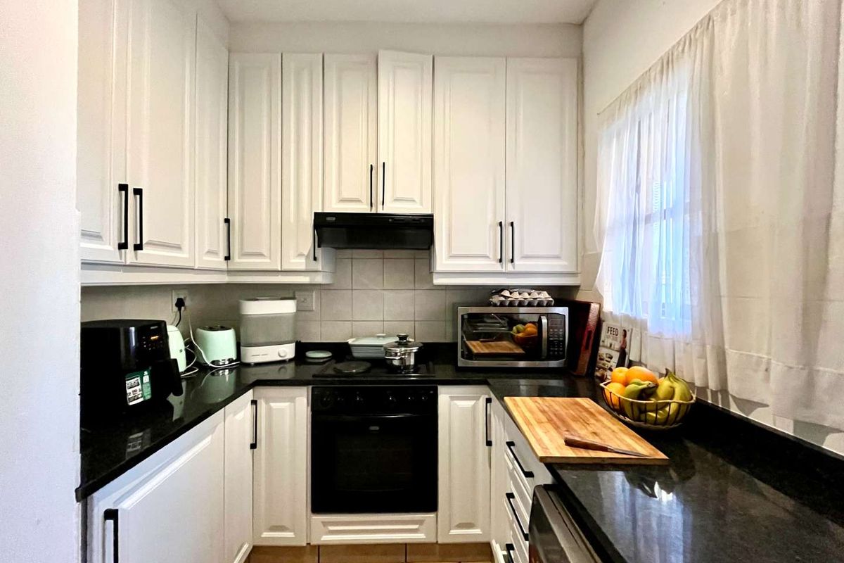 A compact, functional kitchen featuring white cabinetry, black granite countertops, and integrated cooking appliances with a tiled backsplash and floor.