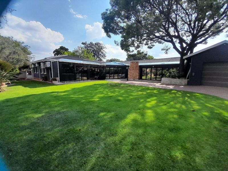 Rear view of the property featuring a large lawn, paved patio area, and dark-painted exterior walls with visible roof maintenance in progress.