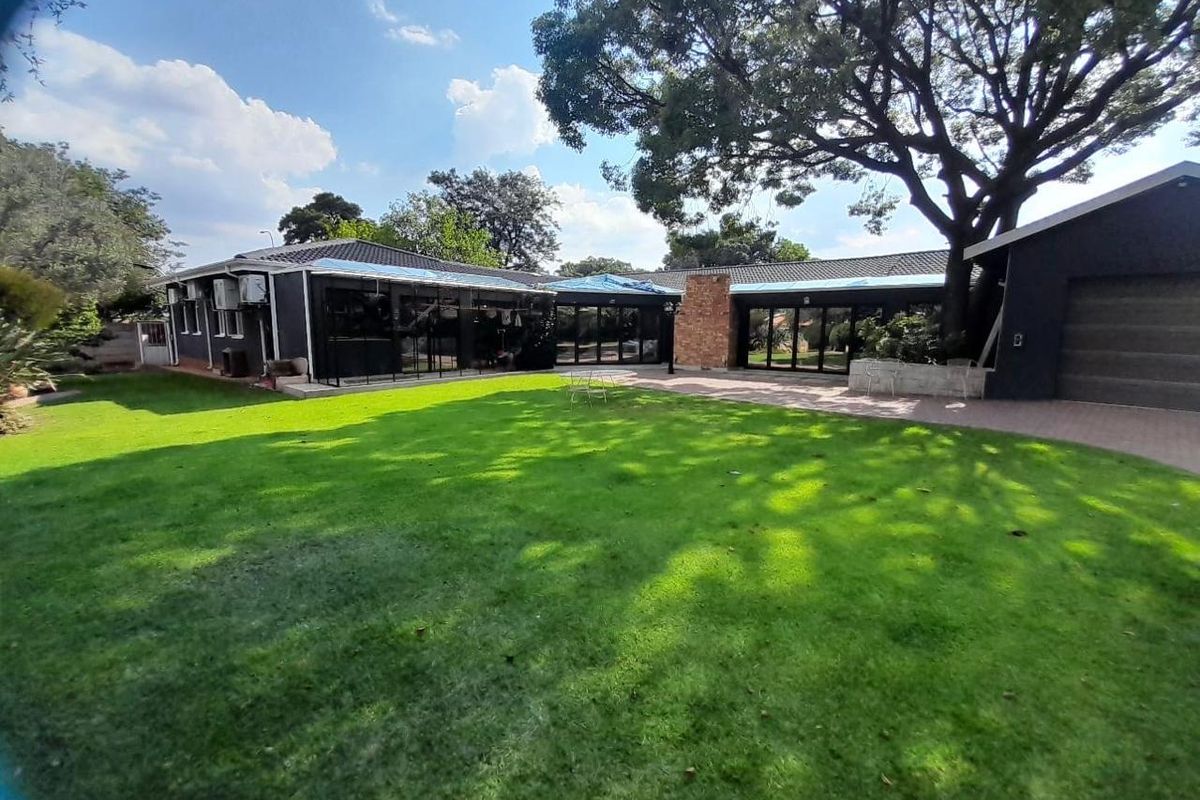 Rear view of the property featuring a large lawn, paved patio area, and dark-painted exterior walls with visible roof maintenance in progress.