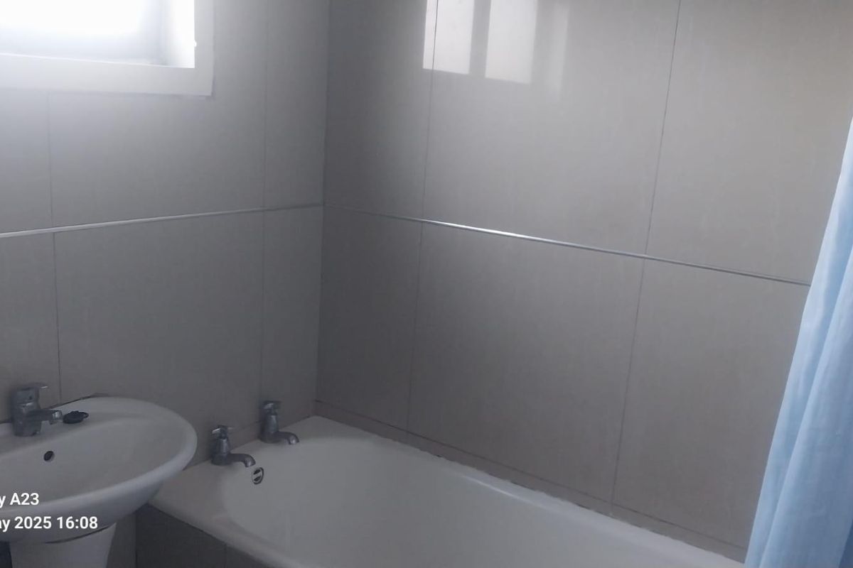 A functional bathroom featuring a pedestal basin, bathtub with chrome taps, and neutral ceramic wall tiling.