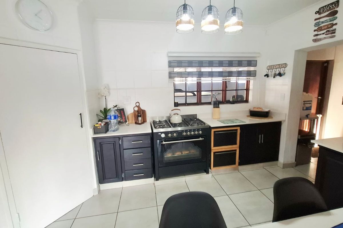 A functional kitchen featuring dark cabinetry, a gas stove with oven, tiled flooring, and modern pendant lighting, providing a practical workspace.