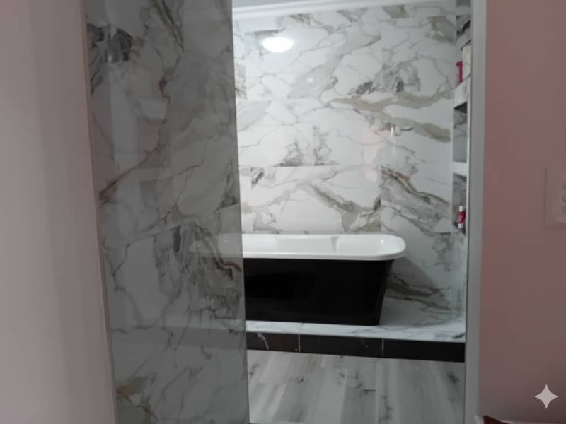 A modern bathroom featuring a sleek freestanding bathtub set against elegant marble-look wall tiles with convenient recessed shelving.