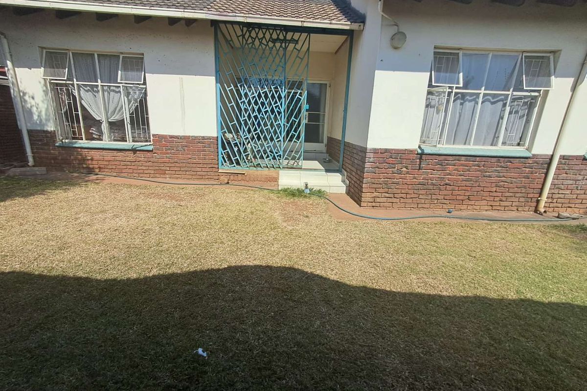 Rear view of the house featuring a brick and plaster facade, security gate at the entrance, and a private garden area.