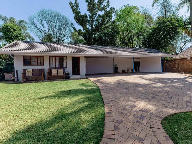 Front exterior view of the property featuring a paved driveway, covered carport area, and established garden surroundings.