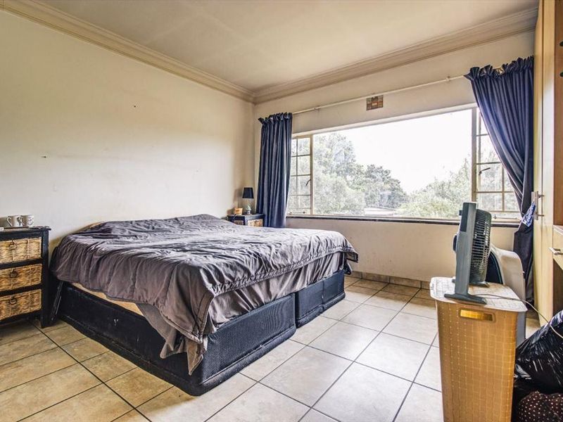 A bedroom featuring tiled flooring, built-in cupboards, and a large window providing natural light and garden views.