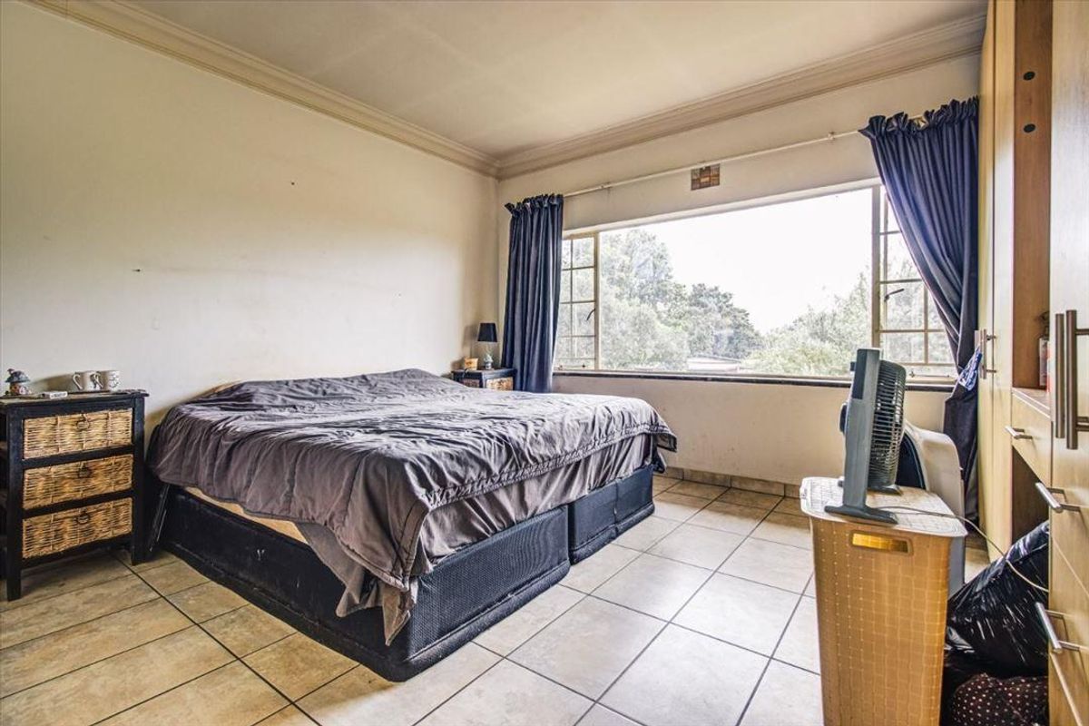 A bedroom featuring tiled flooring, built-in cupboards, and a large window providing natural light and garden views.