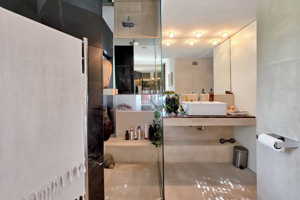 Modern bathroom featuring a glass-enclosed rain shower, stone vanity with a vessel sink, and a heated towel rail.