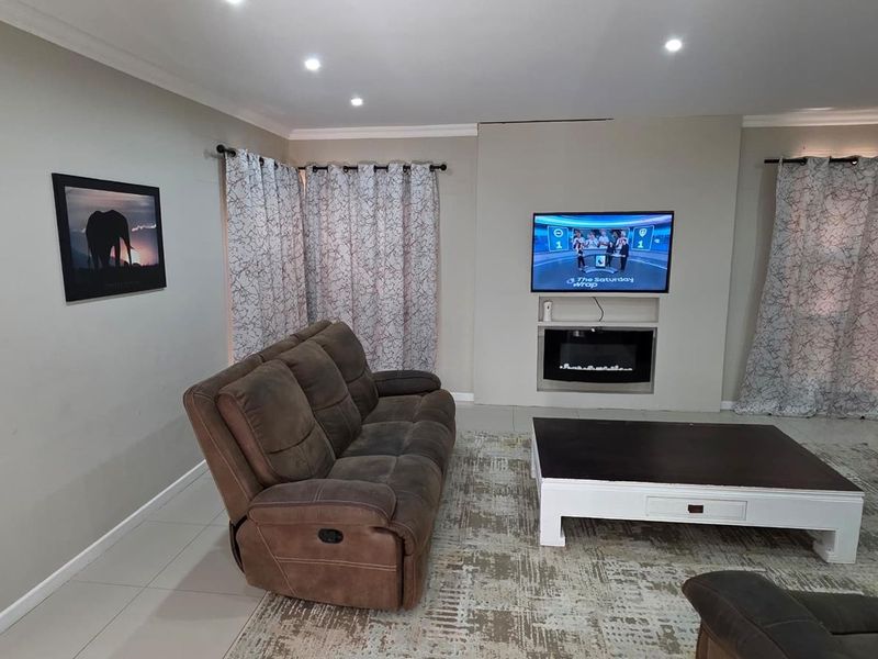 A comfortable living room featuring tiled flooring, recessed downlighting, and a central built-in electric fireplace with a wall-mounted television.
