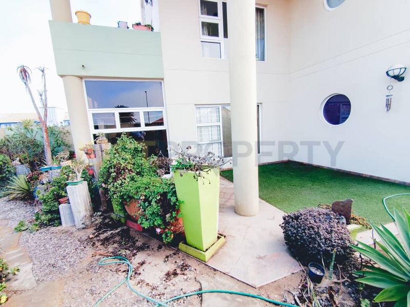 Rear exterior view of the apartment featuring a paved patio area, artificial lawn, and structural architectural elements including a circular window.
