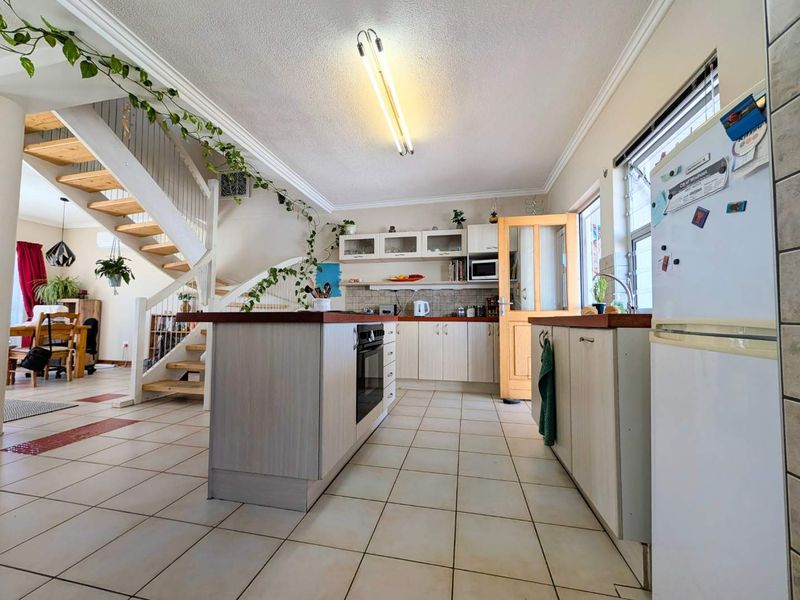 Open-plan kitchen featuring a central island, built-in cabinetry, and tiled flooring, seamlessly connected to the living area and staircase.