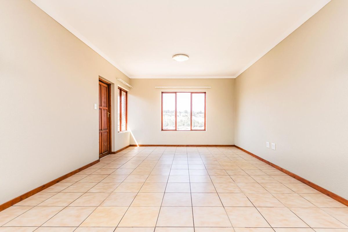 A spacious, empty living area featuring neutral walls, tiled flooring, and wooden window frames, offering a blank canvas for interior design.