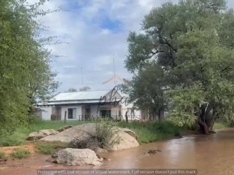 A view of the farm dwelling situated along a riverbank, featuring a traditional structure with a metal roof and natural surroundings.