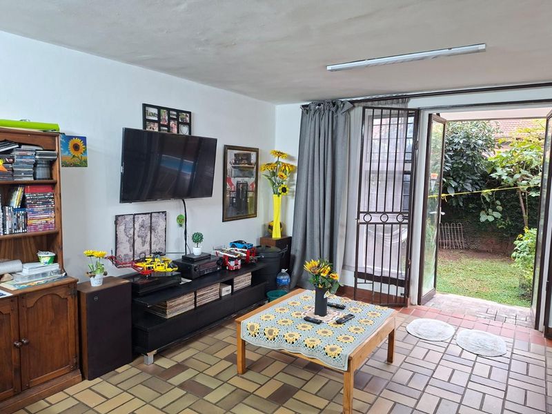 A living room featuring tiled flooring and direct access to the rear garden through double glass doors with an integrated security gate.